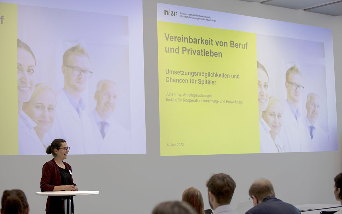 Eine Frau referiert im Stehen vor einer PowerPoint-Präsentation