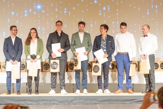 Diplomierte stehen mit ihren Diplomen auf der Bühne