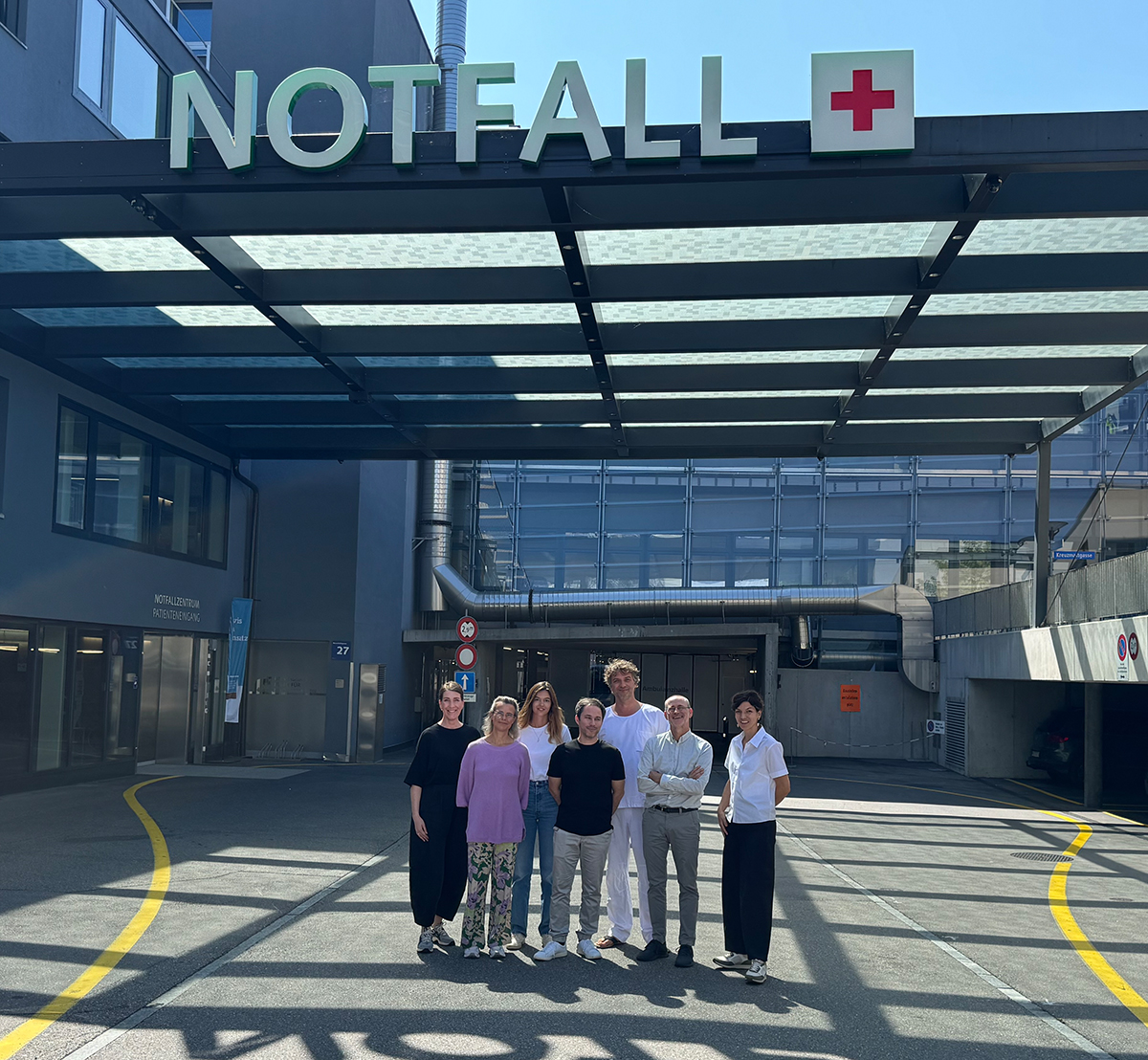 Das Projektteam bestehend aus sieben Personen stehen vor dem Notfall-Eingang eines Krankenhauses.
