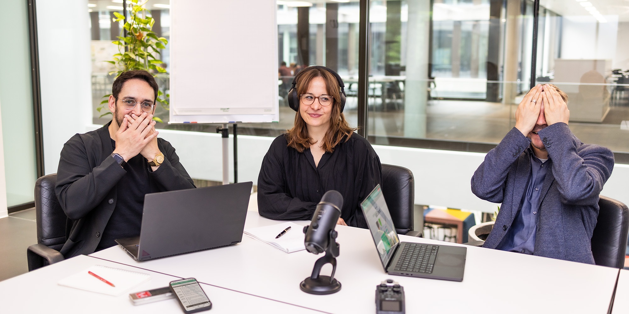 Moderatoren eines Podcasts sitzen an einem Tisch und verzerren die gesichter