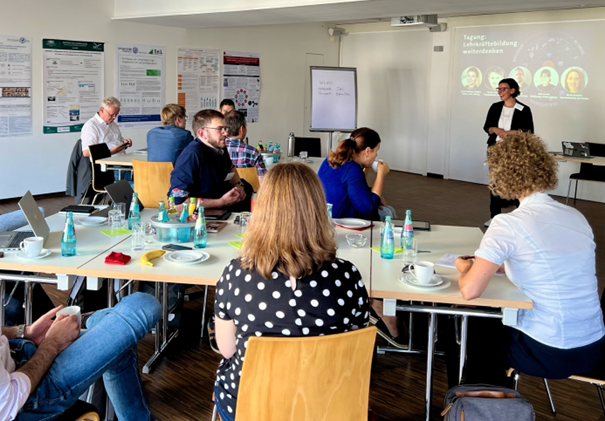 Personen sitzen während einer Präsentation gemeinsam um Tischgruppen