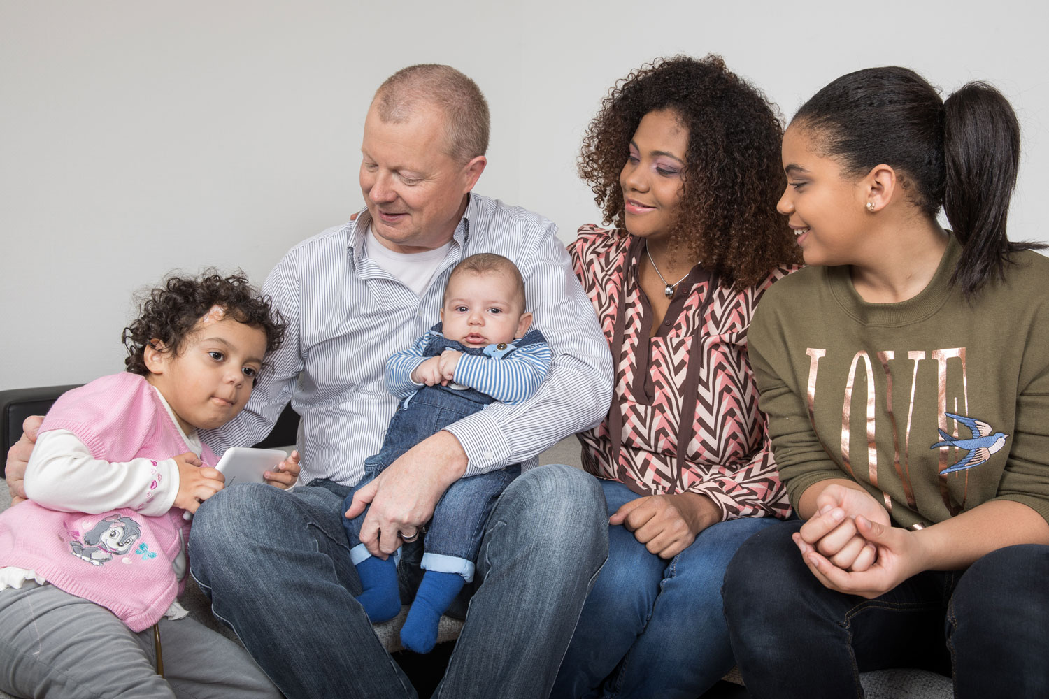 Mutter, Vater und ihre drei Kinder sitzen zusammen auf einem Sofa.