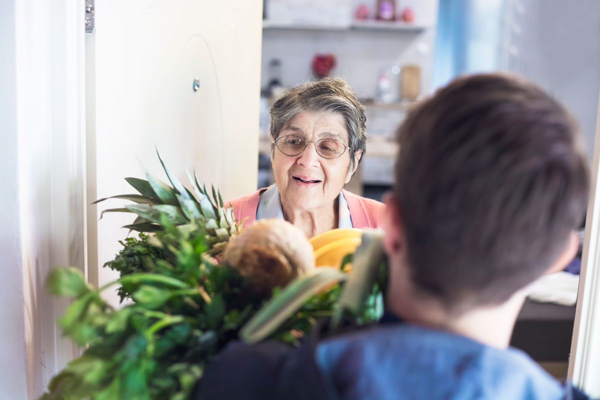 Fotografie: Mann bringt älterer Frau Essen nach Hause. 