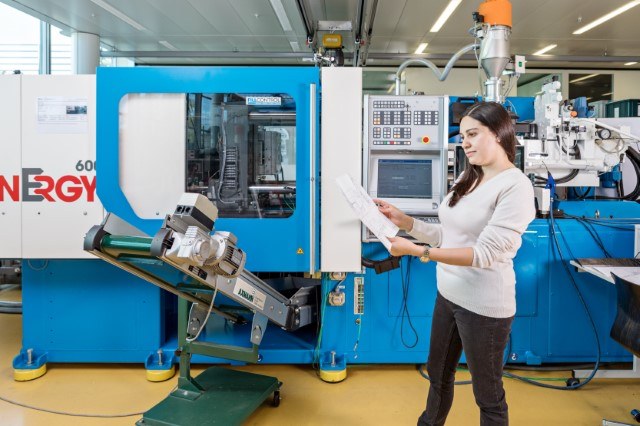 Eine Lernende neben einer Produktionslinie