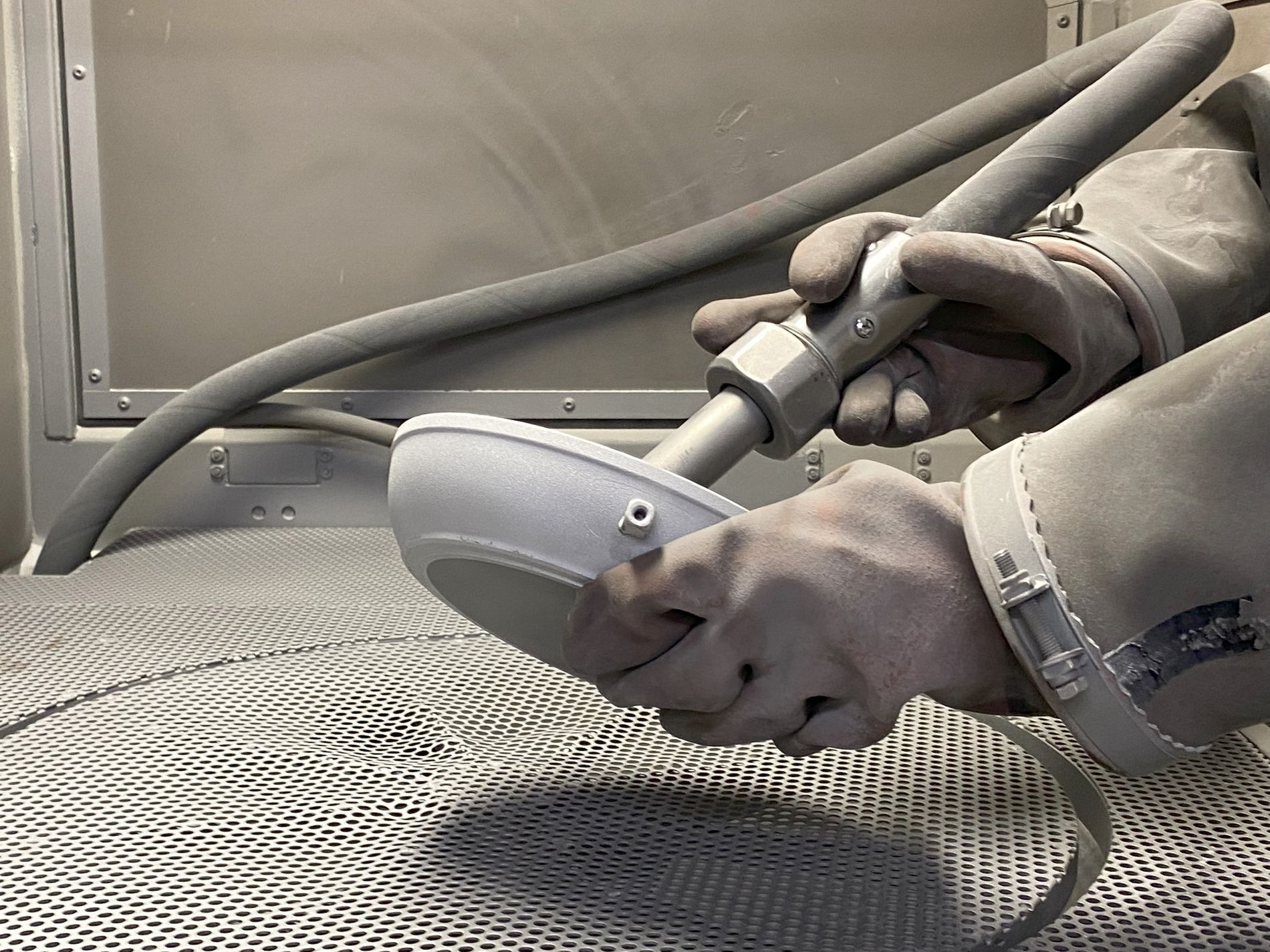 Eine Person mit Handschuh hält die Pfanne und in der anderen Hand ein Schleifgerät, mit dem die alte Beschichtung entfernt wird.