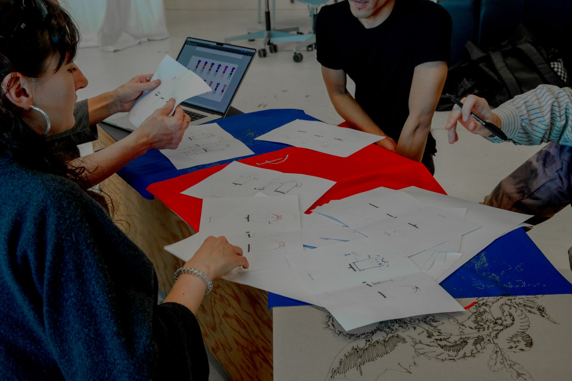 Designphase der Trikots: die Studierendengruppe hat Skizzen von Trikotdesigns ausgelegt. Darunter liegt roter und blauer Stoff in den Farben des FC Basel