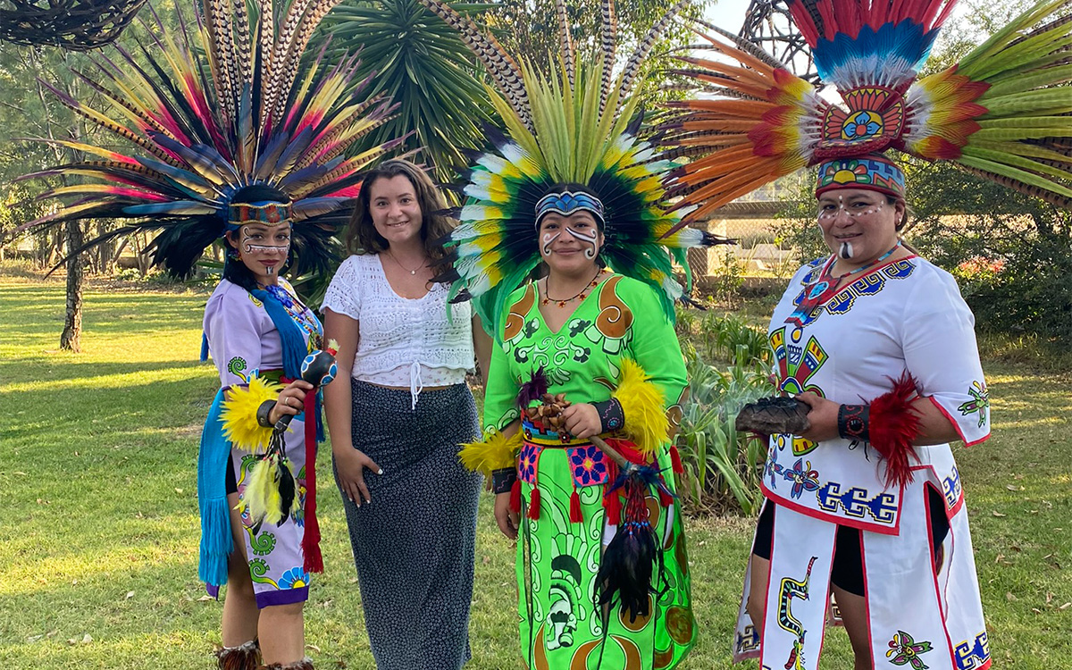 Rosina steht mit drei indigen gekleideten Frauen mit Kopfschmuck auf einer Rasenfläche.